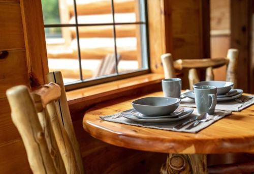 A cozy wooden dining table set with plates and cups, near a window with a view of logs outside.