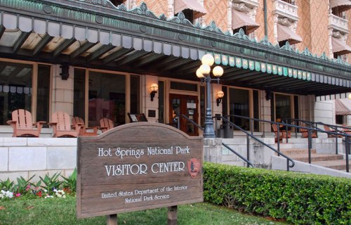 Sign for the Hot Springs National Park Visitor Center in front of a historic building with outdoor seating.