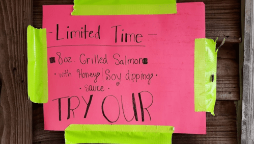 Bright pink sign promoting limited-time 8oz grilled salmon with honey soy dipping sauce.