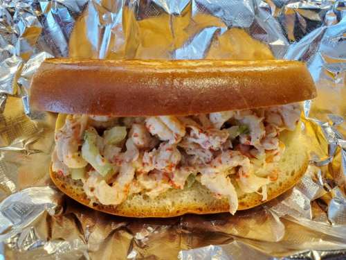 A sandwich filled with shredded chicken and diced vegetables, served on a toasted bun, wrapped in foil.