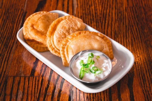 A plate of golden-brown fried pastries served with a small bowl of creamy dipping sauce and green onions.