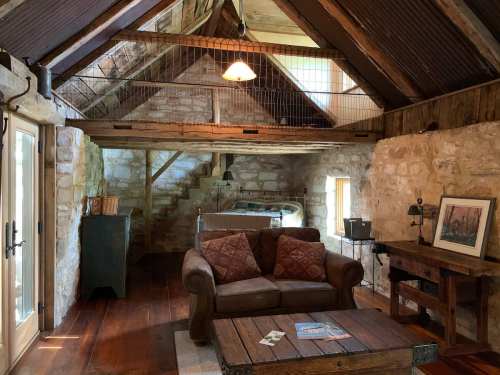 Cozy rustic interior with a stone wall, wooden beams, a sofa, and a small table in a lofted space.