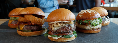 A variety of gourmet burgers on a slate platter, featuring different toppings and styles.