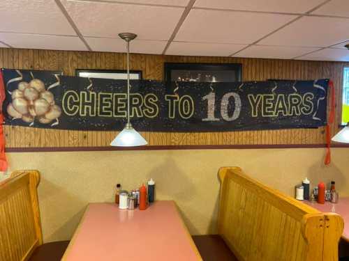 A banner reading "Cheers to 10 Years" hangs in a restaurant, with red ribbons and a cozy dining area in the background.