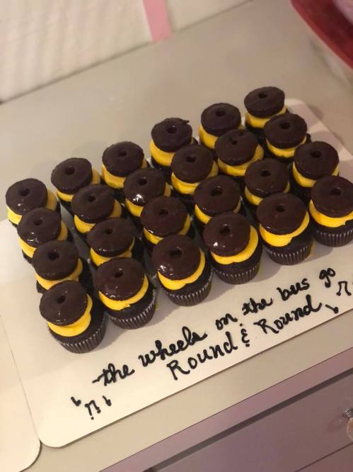 A tray of mini cupcakes resembling hamburgers, topped with yellow frosting and chocolate icing, with a musical note decoration.