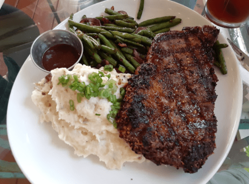A plate with grilled steak, mashed potatoes topped with green onions, and green beans on the side.