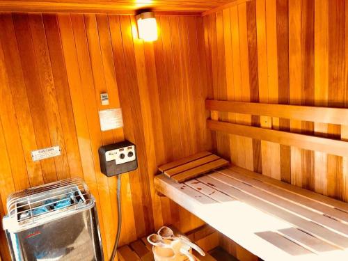 A wooden sauna interior featuring a heater, bench, and slippers on the floor, illuminated by warm lighting.