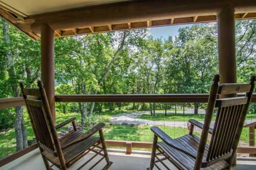 Two wooden rocking chairs on a balcony overlooking a lush green landscape with trees and a winding path.