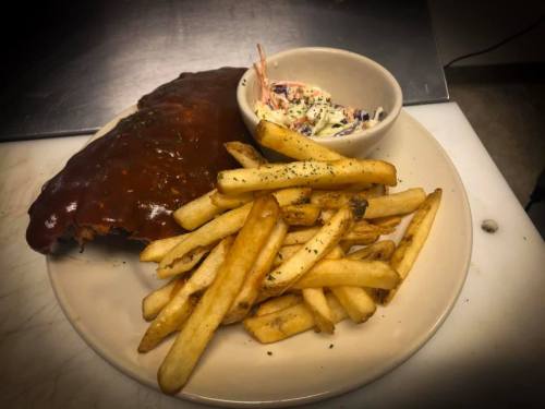 A plate featuring BBQ ribs with a rich sauce, crispy fries, and a small bowl of coleslaw.