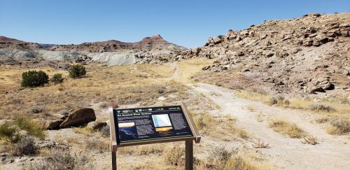 A trail leads through a dry landscape with a sign about the area's geological features and formations.