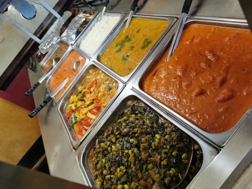 A buffet display featuring various colorful dishes, including curries, vegetables, and rice in metal containers.