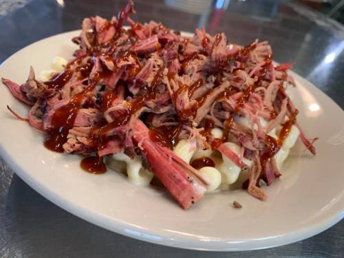 A plate of pulled pork topped with barbecue sauce over a bed of creamy macaroni and cheese.