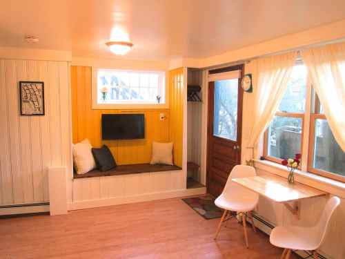 Cozy interior with yellow accent wall, a TV, seating area, and a small dining table by a window.