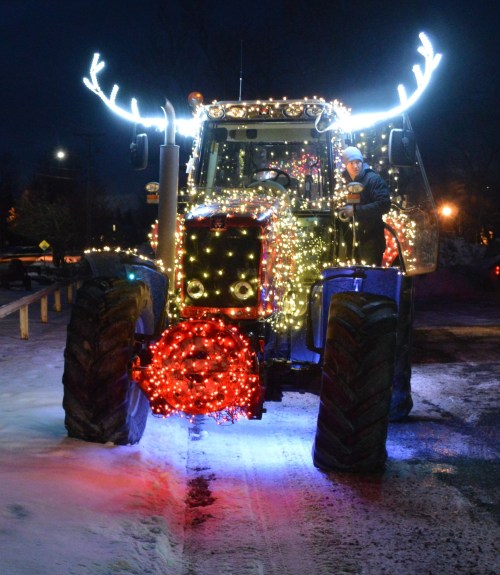 A decorated tractor with lights and antlers, parked at night with snow on the ground.