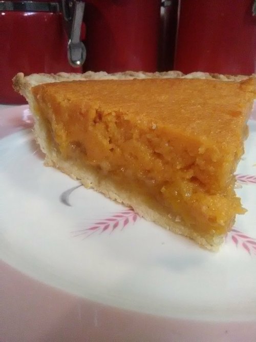A slice of pumpkin pie on a plate, showcasing a golden filling and a flaky crust.