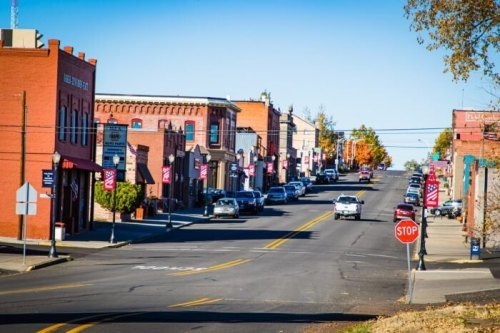 A charming small-town street lined with brick buildings, flags, and parked cars under a clear blue sky.