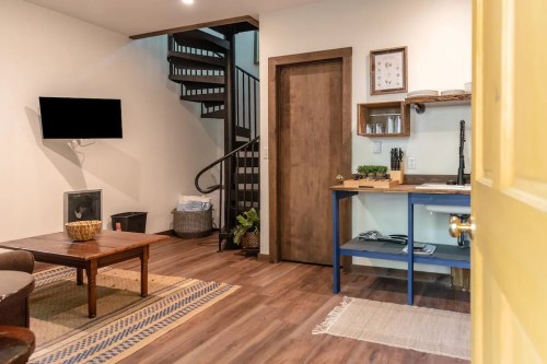 Cozy interior with a staircase, wooden furniture, a TV, and a small kitchen area, viewed from a yellow door.