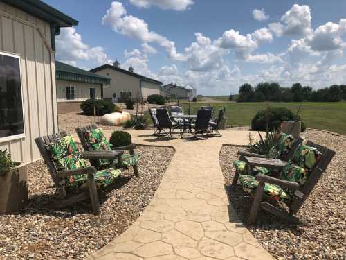 A sunny outdoor patio with colorful chairs, a stone path, and a grassy area in the background under a blue sky.