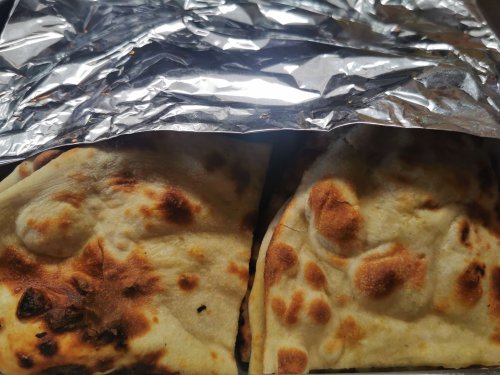 Two pieces of freshly baked naan bread, slightly charred, wrapped in aluminum foil.