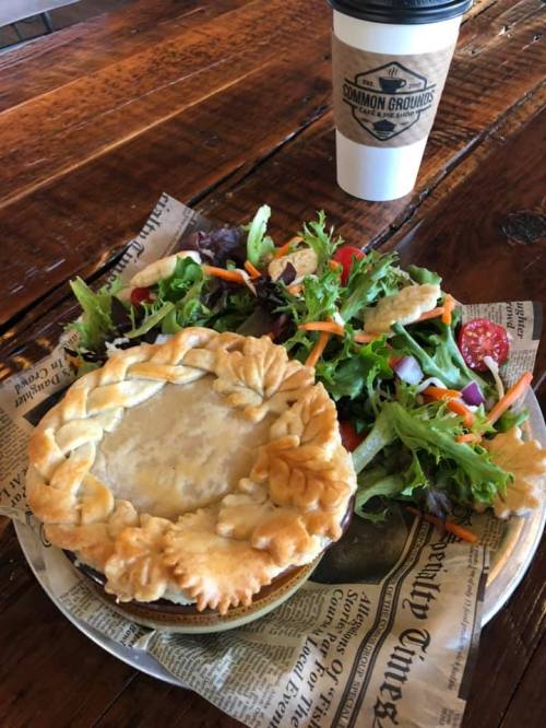 A savory pie on a plate with a side salad and a coffee cup, all set on a wooden table.