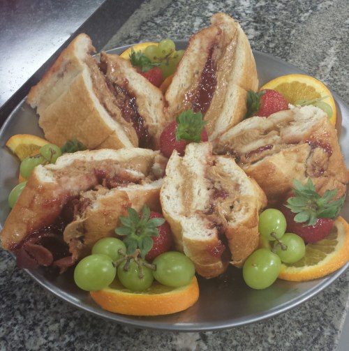 A plate of sliced bread filled with jelly, surrounded by strawberries, grapes, and orange slices.