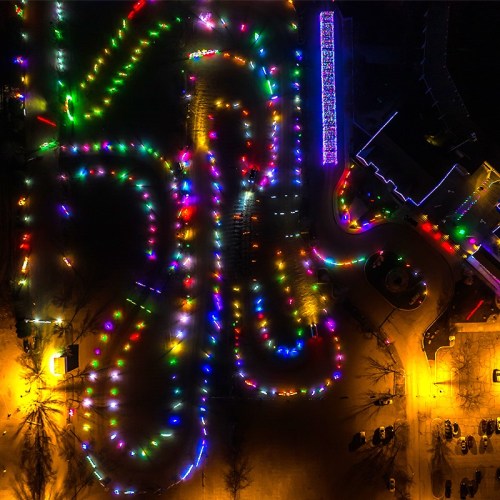 Aerial view of a winding path illuminated with colorful holiday lights in a dark park setting.