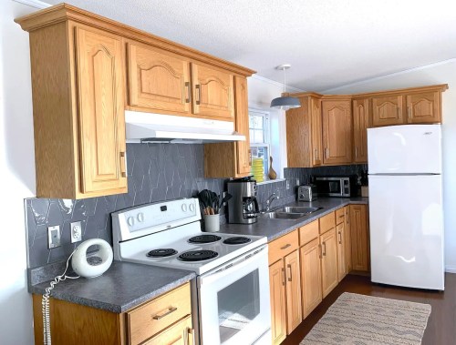 Bright kitchen with wooden cabinets, gray countertops, white appliances, and a modern design.