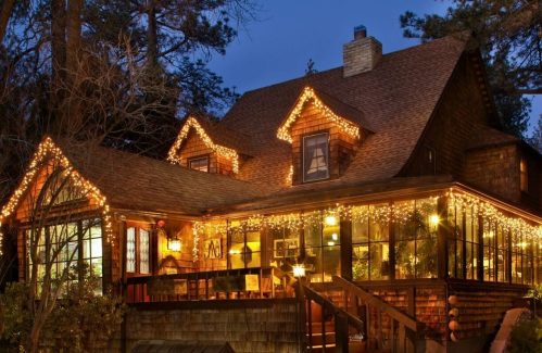 A cozy house adorned with warm, twinkling holiday lights at dusk, surrounded by trees.