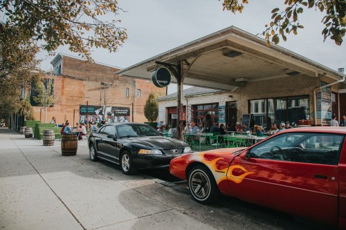 A vibrant street scene with two parked cars in front of a busy café and people enjoying outdoor seating.