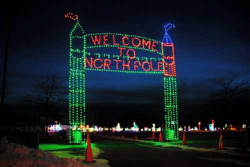 Colorful holiday lights form an archway that reads "Welcome to North Pole" against a twilight sky.