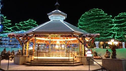 A festive gazebo adorned with lights and decorations, surrounded by snow and illuminated trees at night.