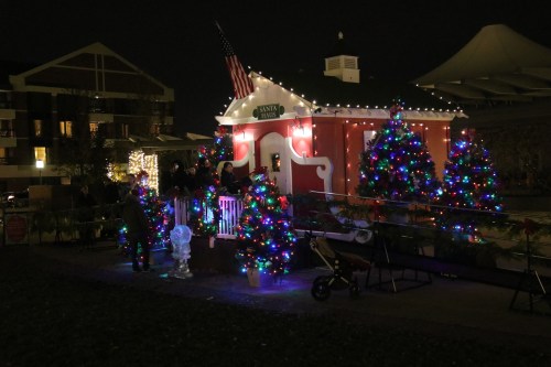 A festive scene with a decorated Santa house and colorful Christmas trees, illuminated at night.