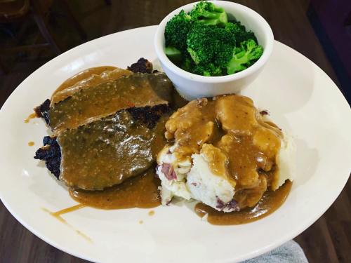 A plate with meatloaf covered in gravy, mashed potatoes with gravy, and a side of steamed broccoli.