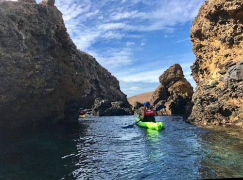 A person kayaking through rocky formations under a blue sky with scattered clouds.