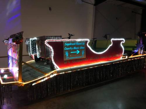 A brightly lit float decorated for a country music show, featuring a sleigh design and colorful lights.