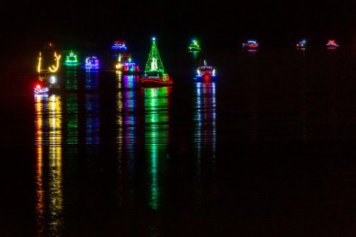 Colorful boats adorned with lights reflect on dark water, creating a festive nighttime scene.