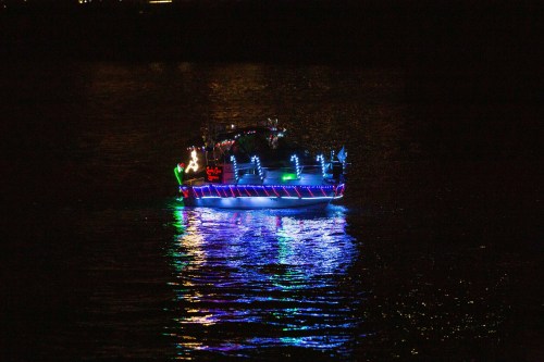 A brightly lit boat glides across dark waters, reflecting colorful lights in the night.