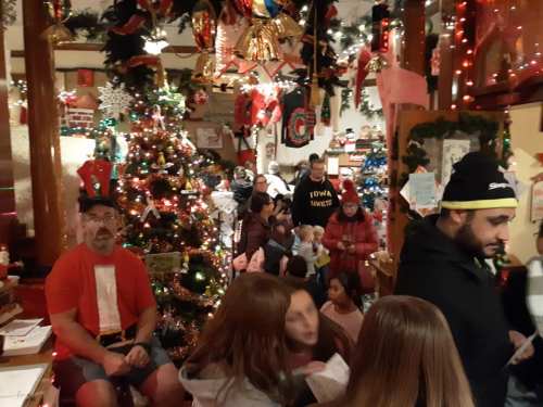 A festive indoor scene with a decorated Christmas tree, people mingling, and holiday decorations all around.
