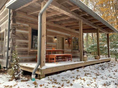 A cozy wooden cabin porch covered in snow, with a table and chairs surrounded by autumn leaves.