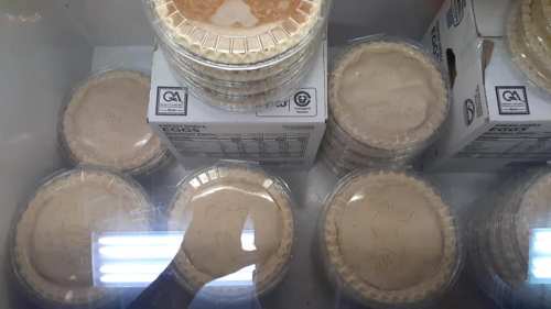 A display of stacked, clear plastic containers holding pie crusts in a freezer.