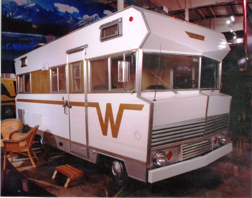 A vintage RV with a white and wood-paneled exterior, featuring large windows and a distinctive "W" logo on the front.