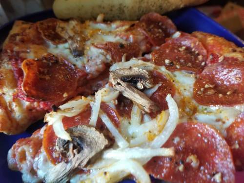 Close-up of two slices of pepperoni pizza topped with onions and mushrooms, served on a blue plate.