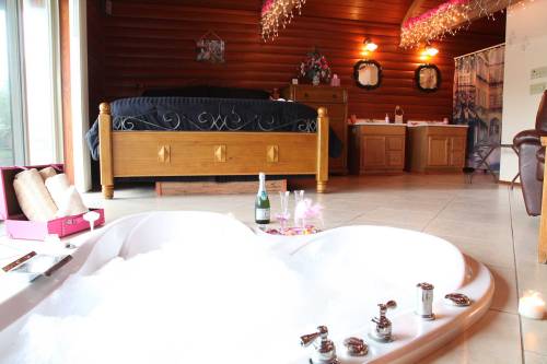 A cozy room featuring a heart-shaped jacuzzi, a bed, and romantic decor with champagne and glasses nearby.