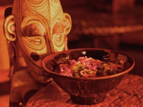 A decorative mask beside a bowl of colorful food, featuring noodles and purple cabbage, in warm lighting.