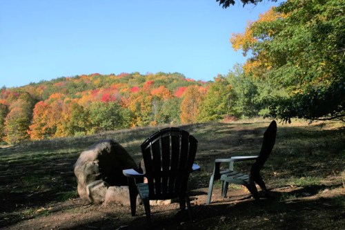 Two chairs sit in a serene outdoor setting, overlooking a colorful autumn landscape with vibrant foliage.