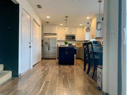 Modern kitchen with white cabinets, stainless steel appliances, a dark island, and wooden flooring. Bright and spacious layout.