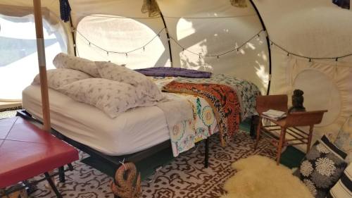 Cozy tent interior with a bed, decorative blankets, pillows, and a small chair, creating a warm, inviting atmosphere.