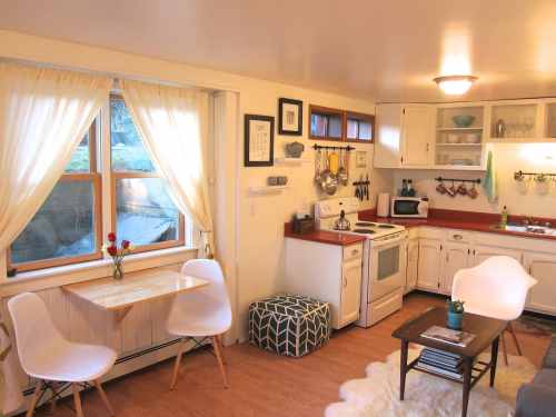 Cozy kitchen with white cabinets, a small dining table, two chairs, and natural light from large windows.