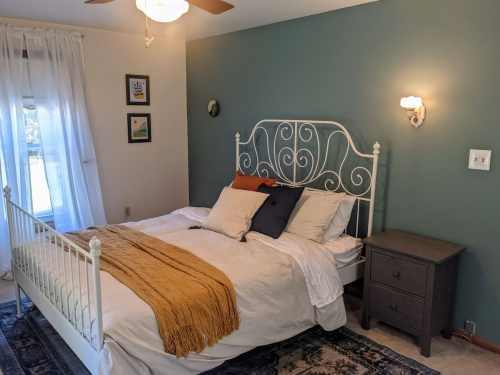 Cozy bedroom featuring a white metal bed, decorative pillows, a nightstand, and a window with sheer curtains.