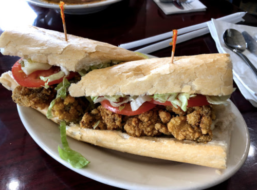 A sandwich with fried chicken, lettuce, tomato, and mayonnaise, served on a toasted baguette with toothpicks.